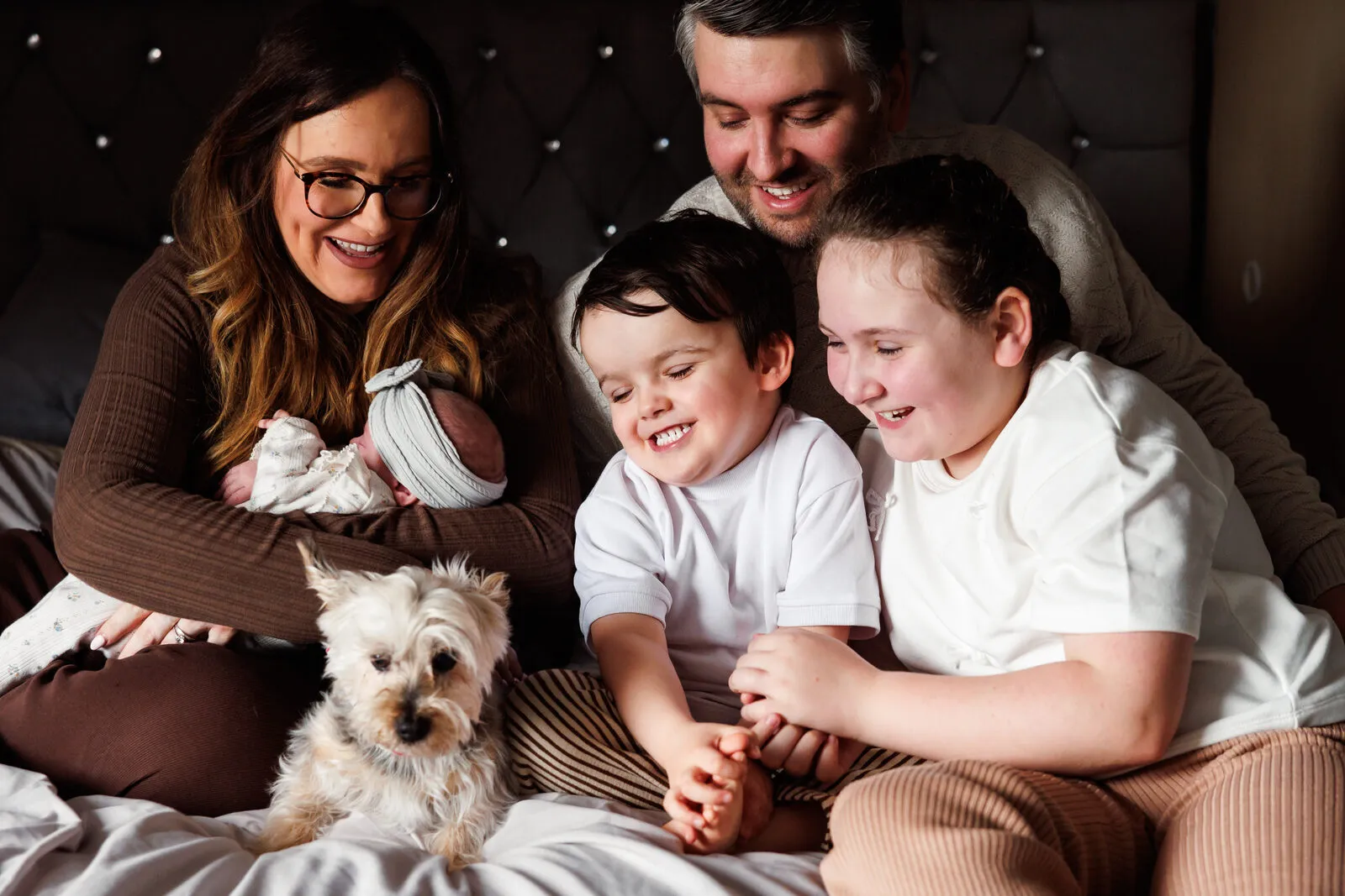 Emma and her family cuddled together on the bed with their newborn and dog