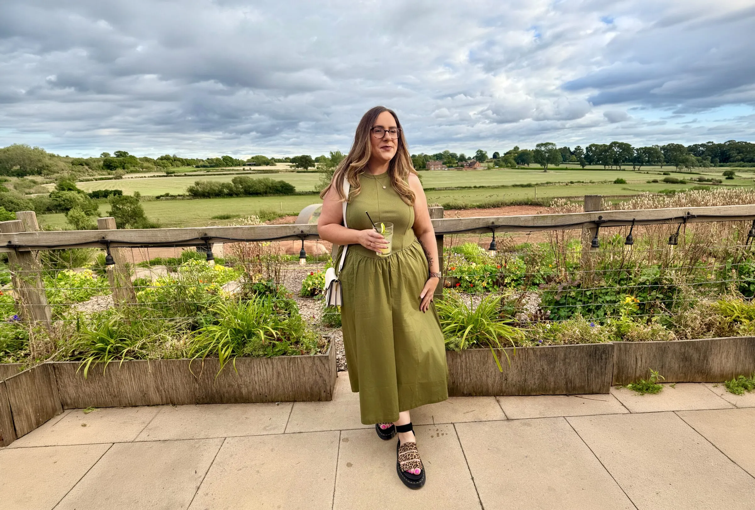 Emma in an olive midi dress on a countryside terrace