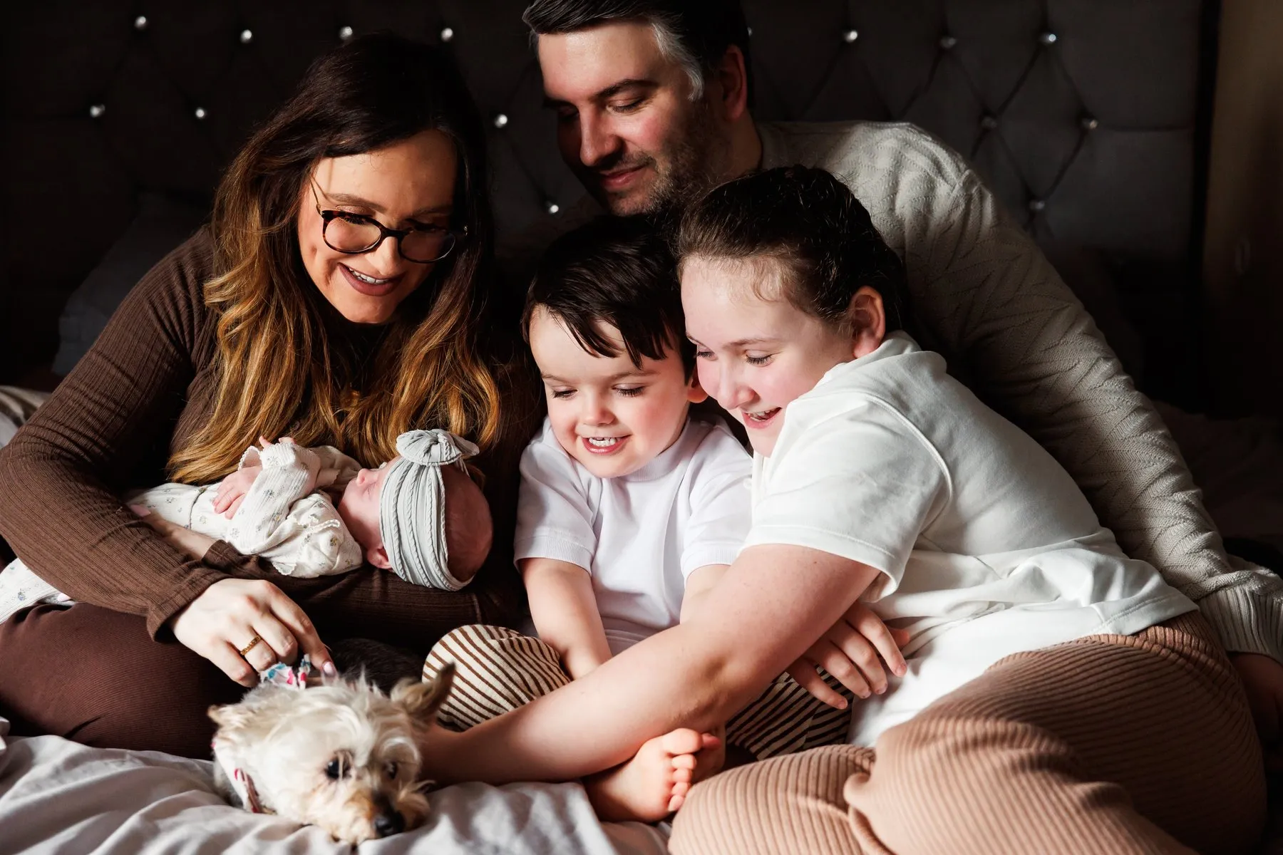 Emma and her family cuddled together on a bed meeting the new baby