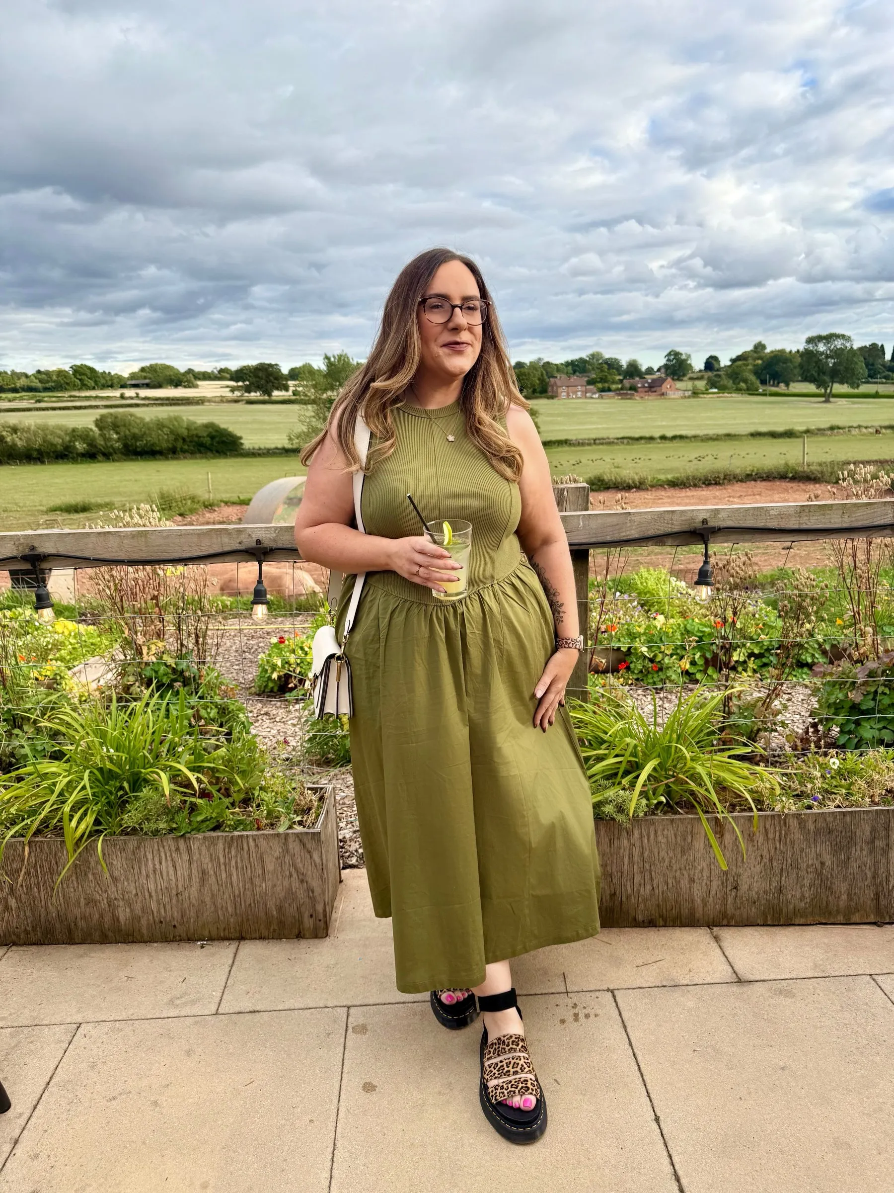 Emma wearing an olive-green midi dress in a countryside garden